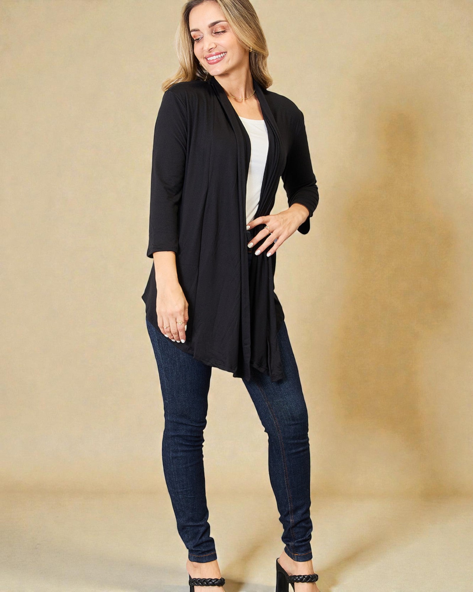 Woman wearing a black cardigan over a white top and blue jeans on a beige background