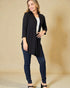 Woman wearing a black cardigan over a white top and blue jeans on a beige background