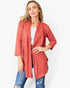A woman modeling a rust-colored, open-front cardigan with three-quarter sleeves over a white top and blue jeans, set against a plain white studio background.