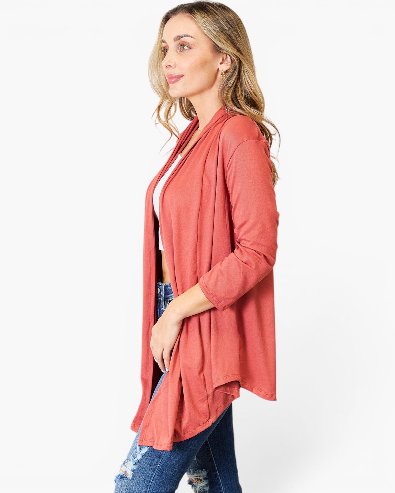 A woman modeling a lightweight, open-front cardigan in a muted coral pink color, styled with a white top and blue jeans against a plain white studio background.