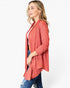 A woman modeling a lightweight, open-front cardigan in a muted coral pink color, styled with a white top and blue jeans against a plain white studio background.