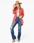 A woman modeling a rust-colored open-front cardigan over a white crop top, paired with distressed blue jeans and tan boots, on a light gray background.