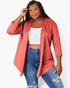 A plus-size model wearing a coral pink open-front cardigan over a white crop top and blue distressed jeans, posed against a light gray studio background.