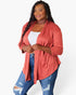 A plus-size woman modeling a coral pink open-front cardigan over a white tank top and distressed blue jeans, photographed against a clean white studio background.