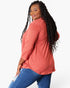 A woman modeling a three-quarter sleeve coral pink button-up shirt with blue jeans, shown from a three-quarters back view against a plain white background.