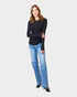 Woman wearing a black long-sleeve top and blue jeans on a white background