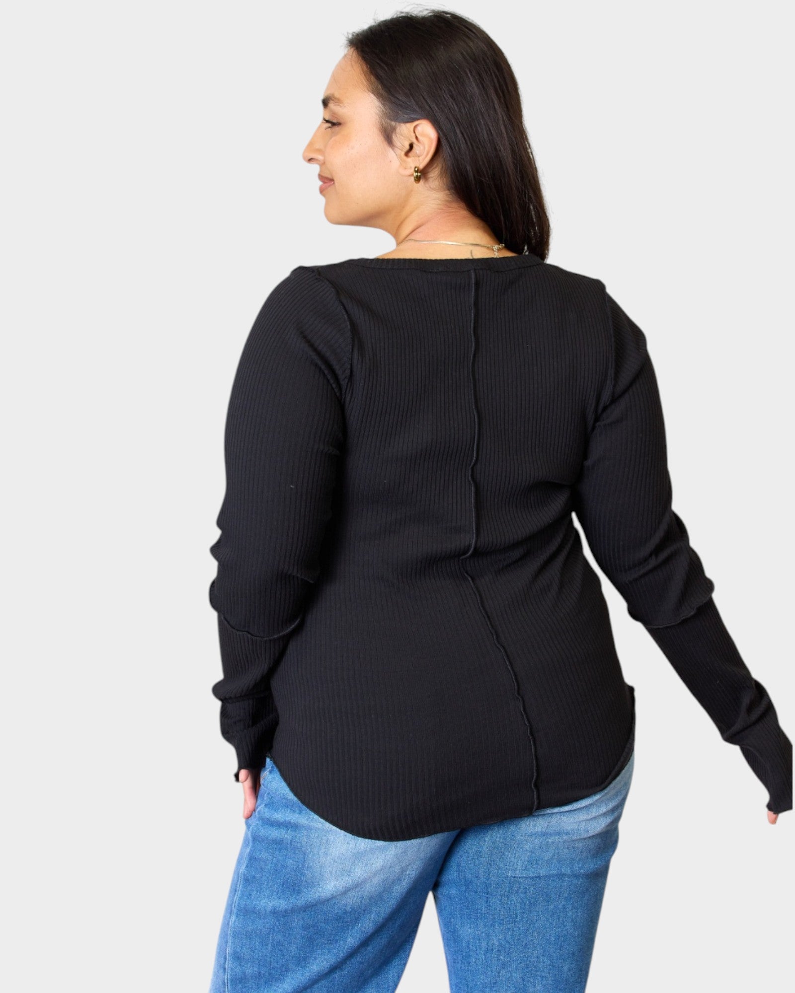 Person wearing a black long-sleeve top and blue jeans on a white background
