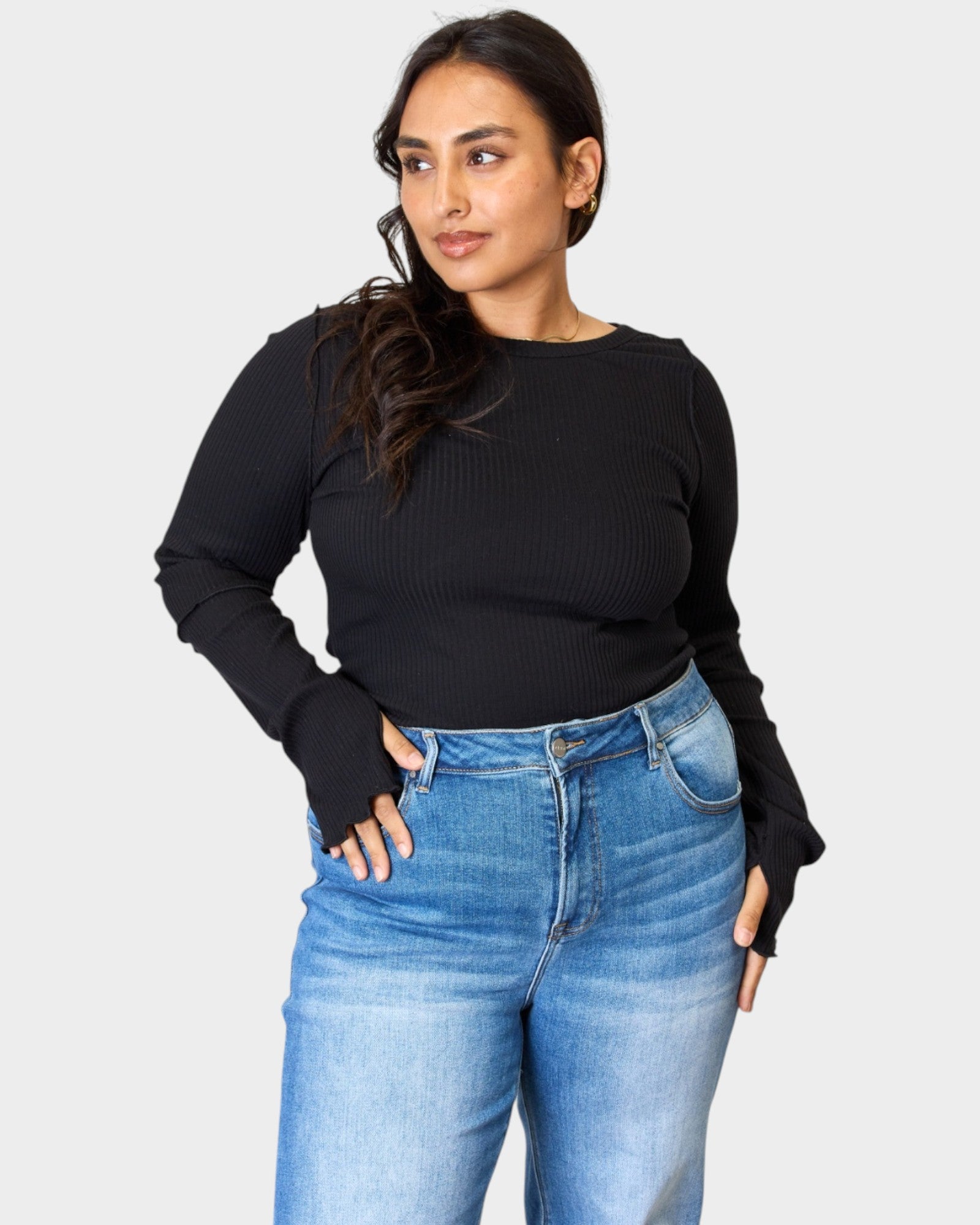 Woman wearing a black sweater and blue jeans on a plain background