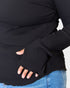 Person wearing a black ribbed sweater with fingerless gloves and blue jeans on a light gray background