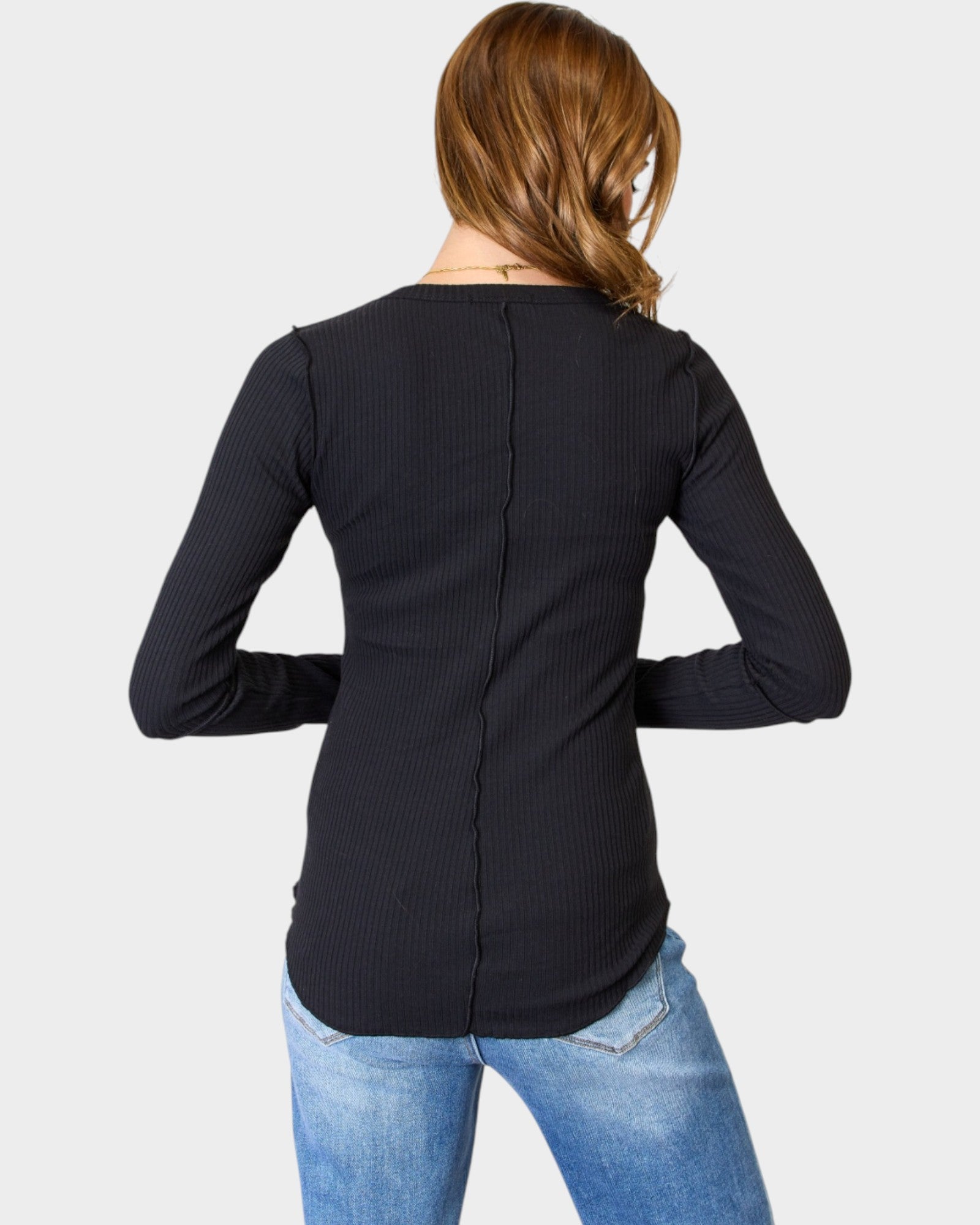 Person wearing a black long-sleeve top and blue jeans on a light gray background