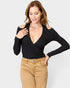 Woman wearing a black long-sleeve top and beige pants on a white background