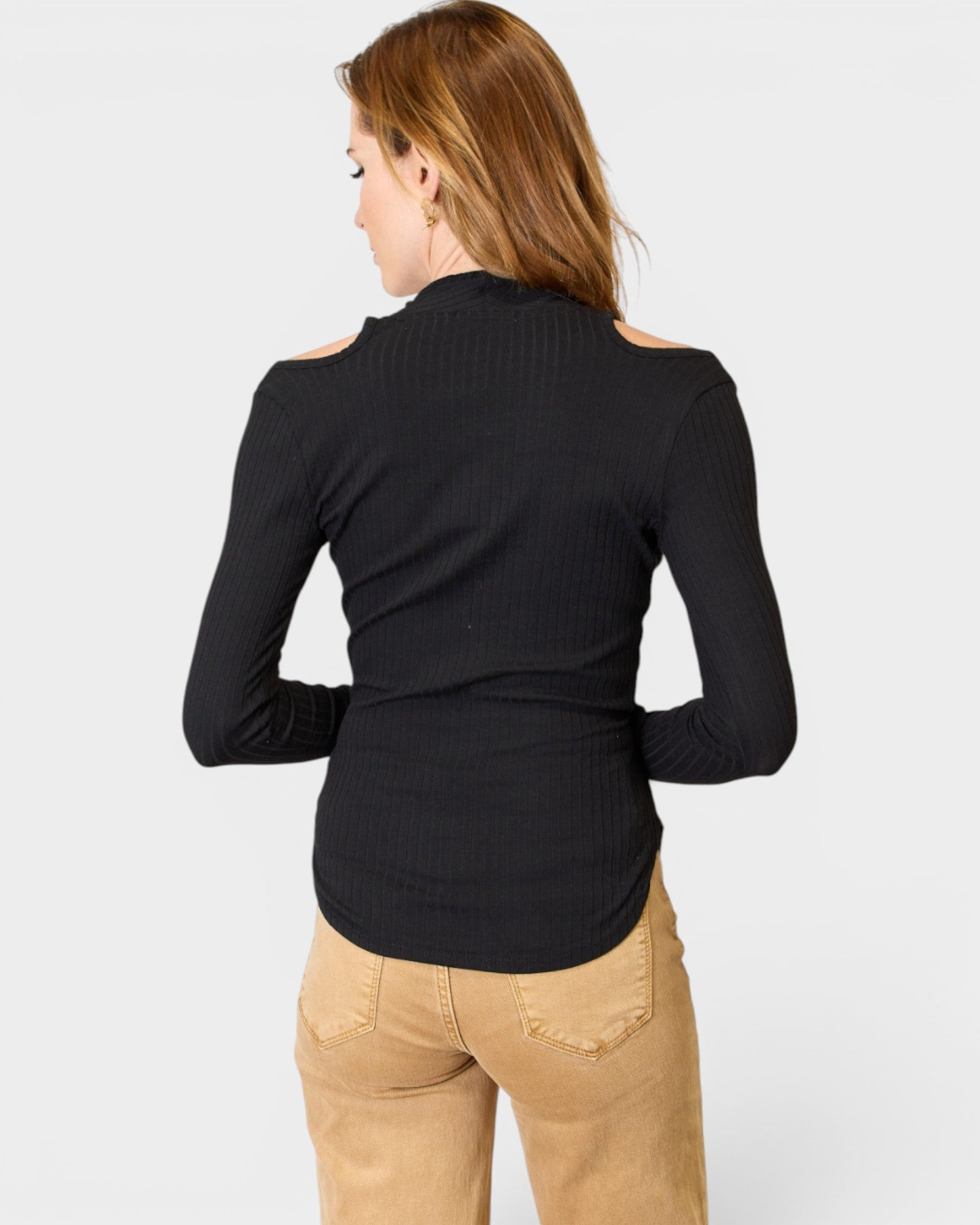 Woman wearing a black long-sleeve top and beige pants on a white background