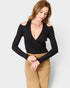 Woman wearing a black long-sleeve top and beige pants on a light gray background