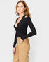 Woman wearing a black long-sleeve top and beige pants on a white background