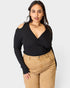 Woman wearing a black top and beige pants against a white background