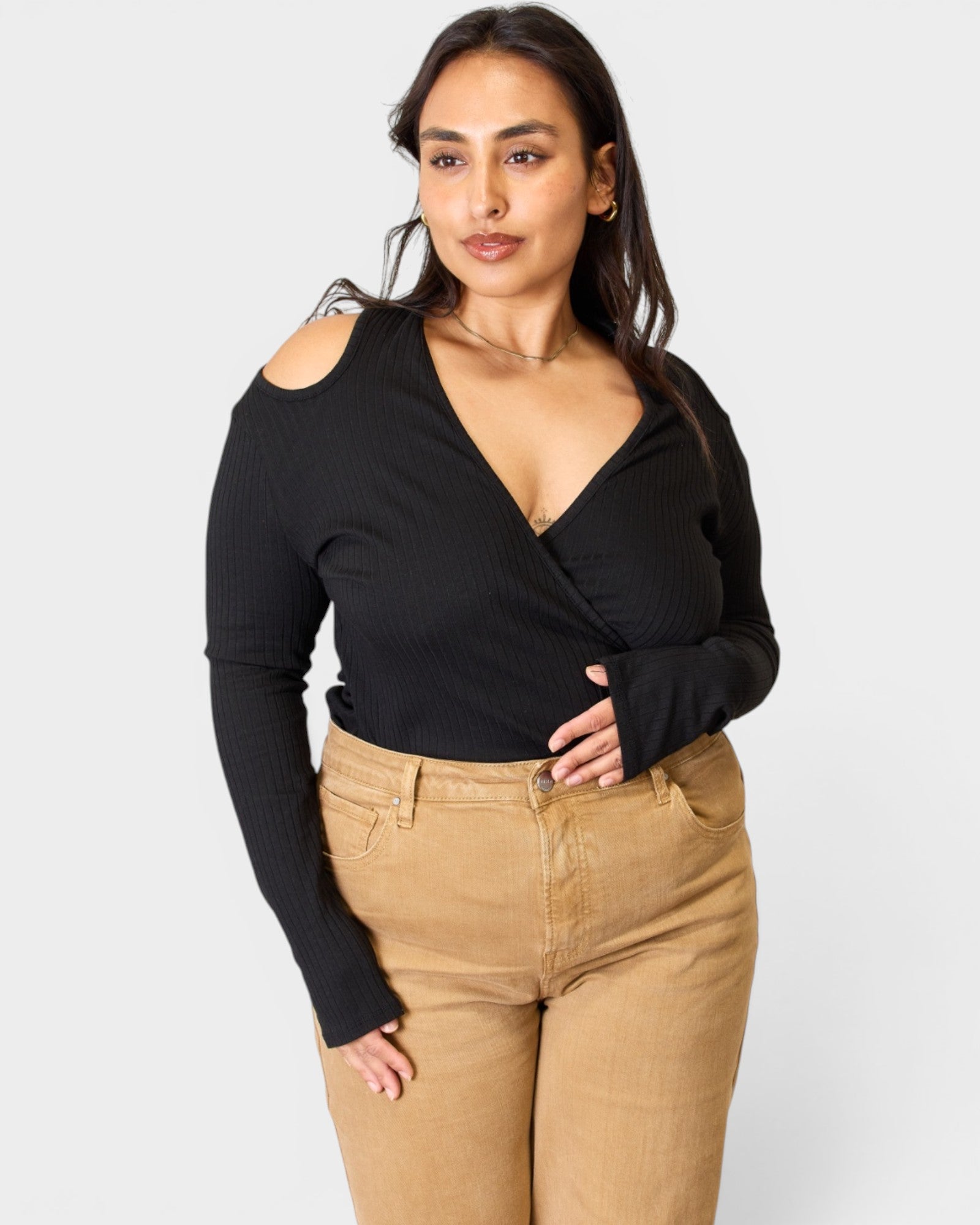 Woman wearing a black long-sleeve top and tan pants on a white background