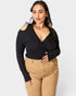 Woman wearing a black long-sleeve top and tan pants on a white background
