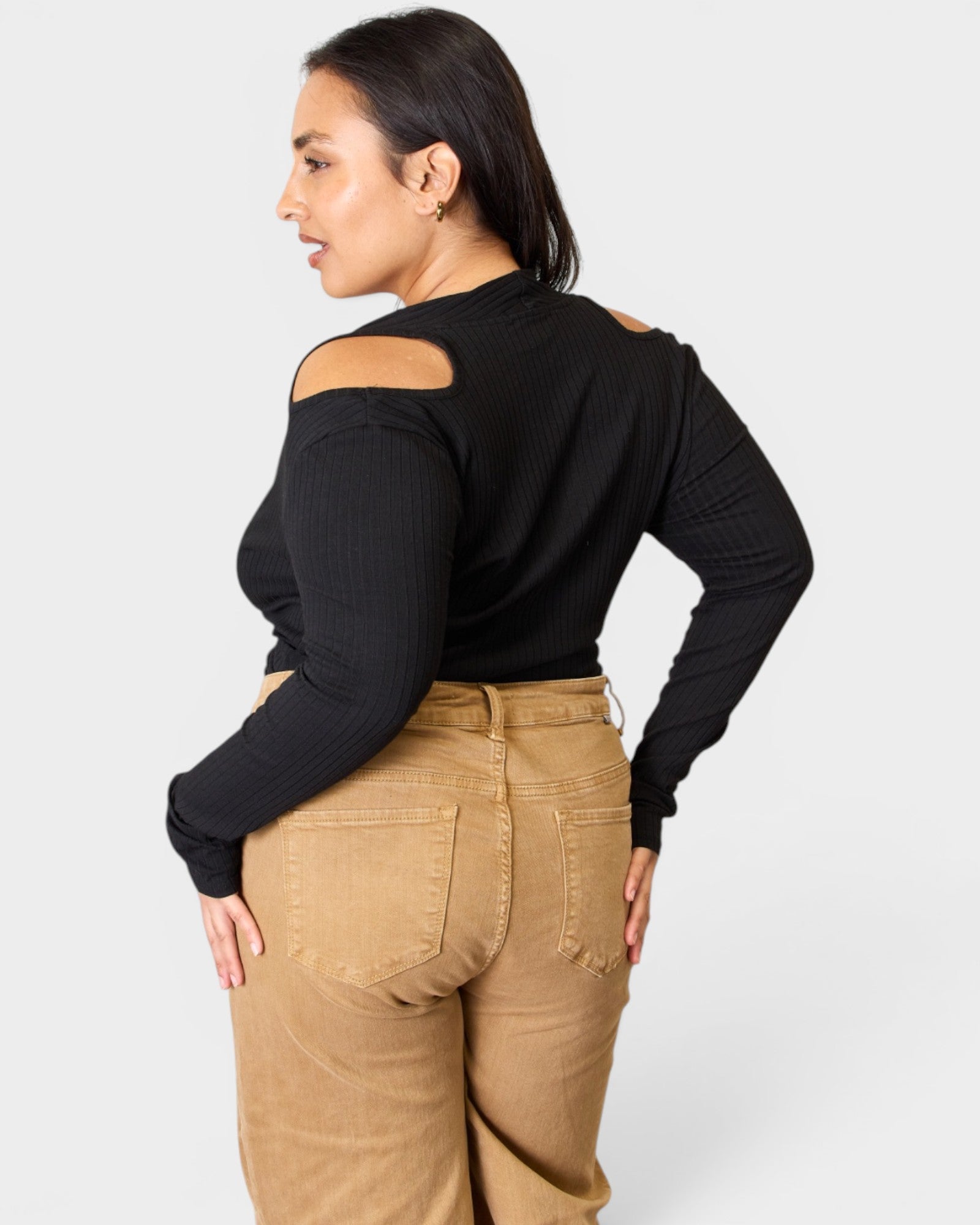 Woman wearing a black long-sleeve top with cut-out shoulders and beige pants on a white background