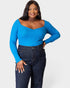 Woman wearing a blue ribbed long-sleeve top and dark jeans on a white background