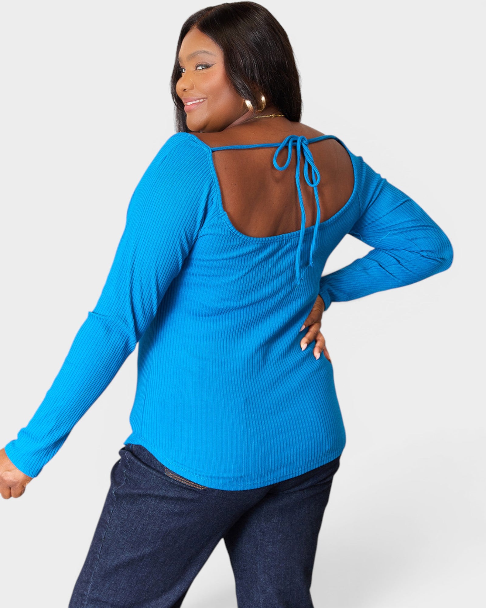 Woman wearing a blue long-sleeve top with open back design on a white background