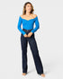 Woman wearing a blue off-shoulder top and dark jeans on a white background