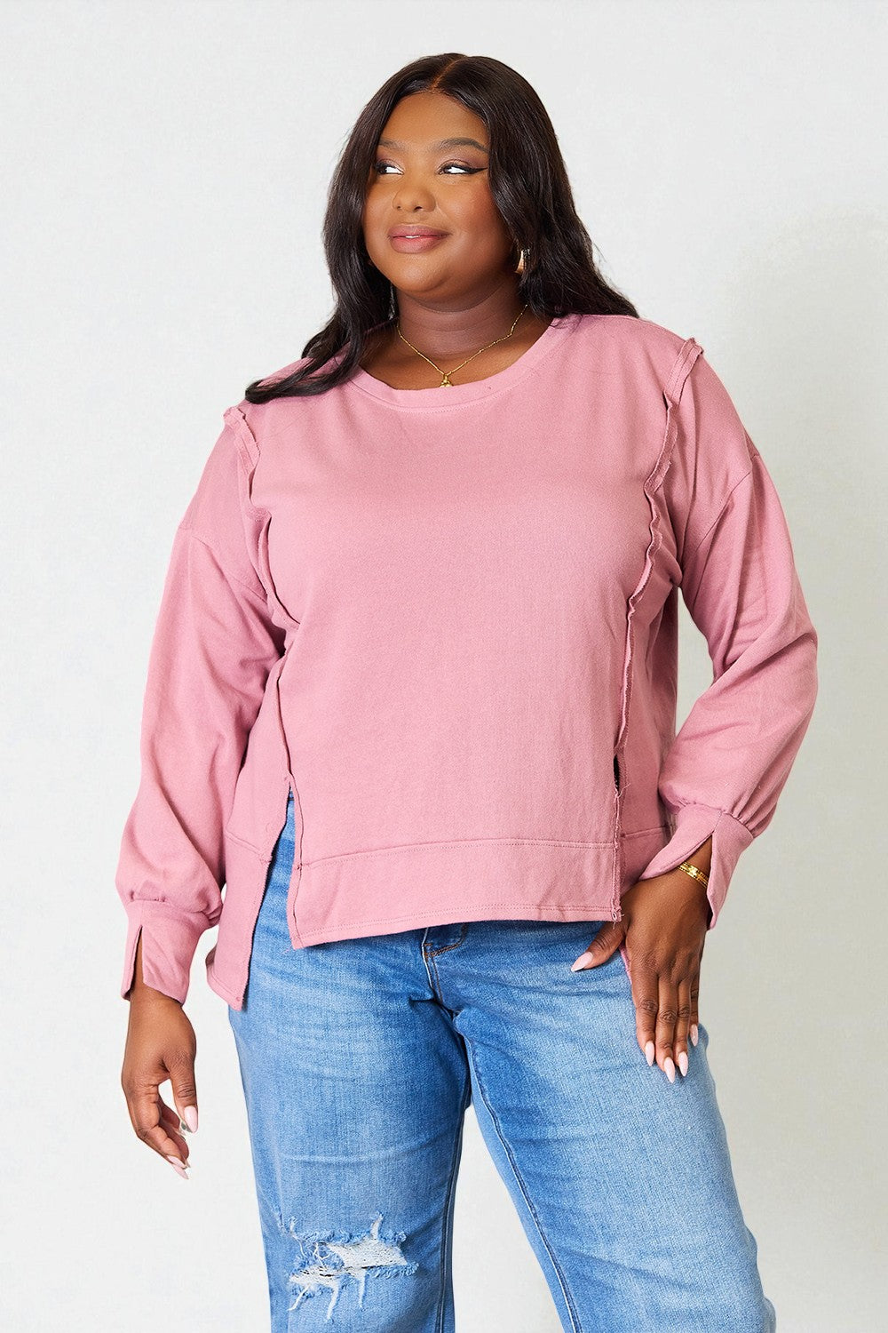 Woman wearing a pink sweatshirt and blue jeans against a white background