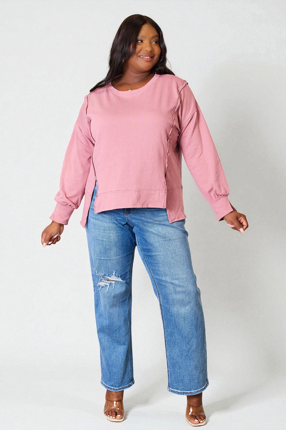Woman wearing a pink sweatshirt and blue jeans on a white background