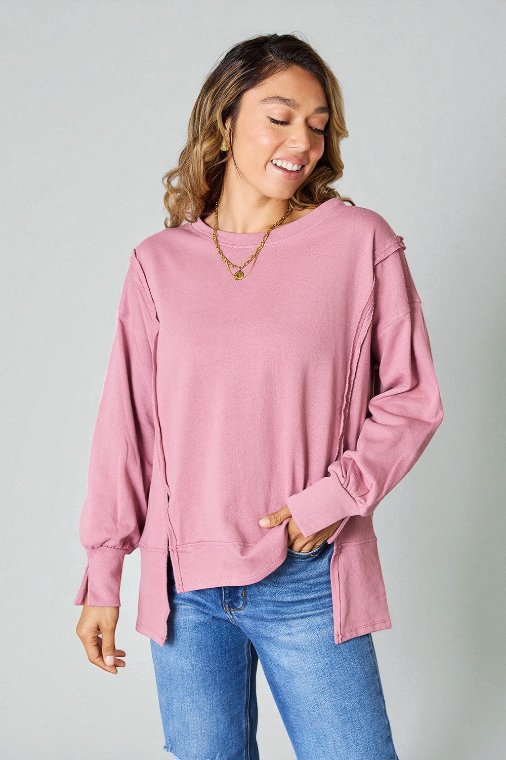 Woman wearing a pink oversized sweater and blue jeans against a plain background