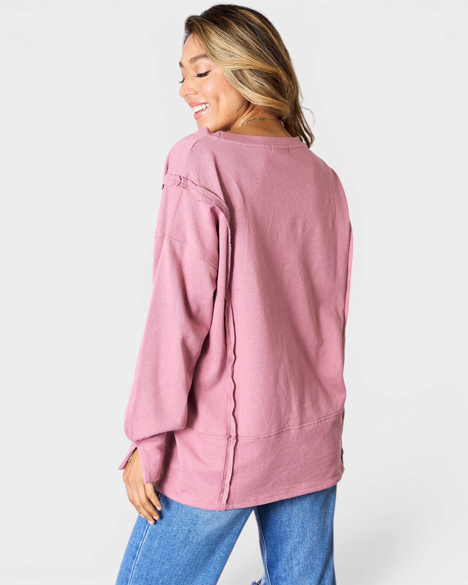 Woman wearing a pink long-sleeve top and blue jeans on a white background