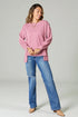 Woman wearing a pink oversized sweater and blue jeans on a plain background