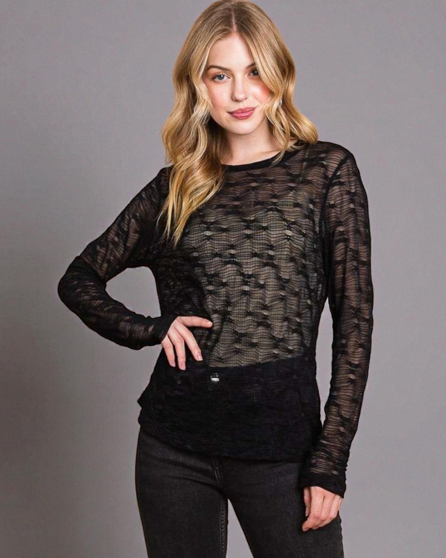 Woman wearing a black sheer top and black pants against a gray background