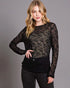 Woman wearing a black sheer top and black pants against a gray background