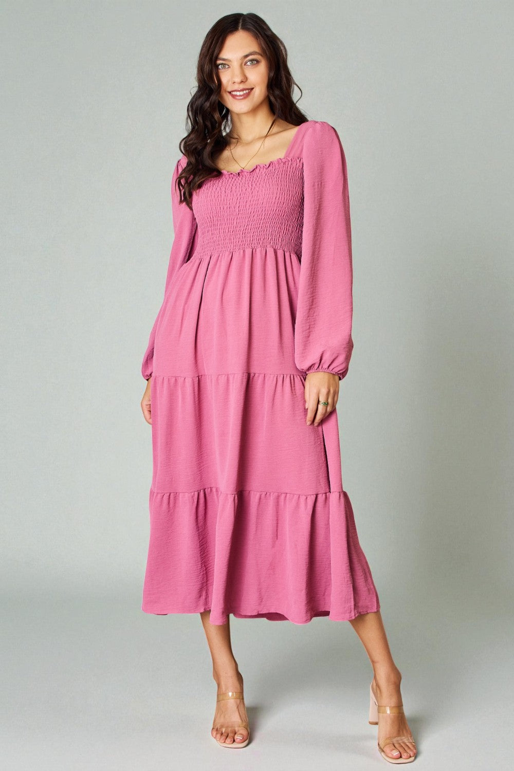 Woman wearing a pink dress with long sleeves on a gray background