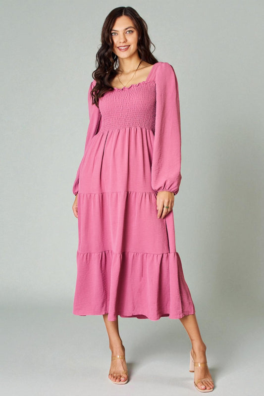 Woman wearing a pink dress with long sleeves on a gray background