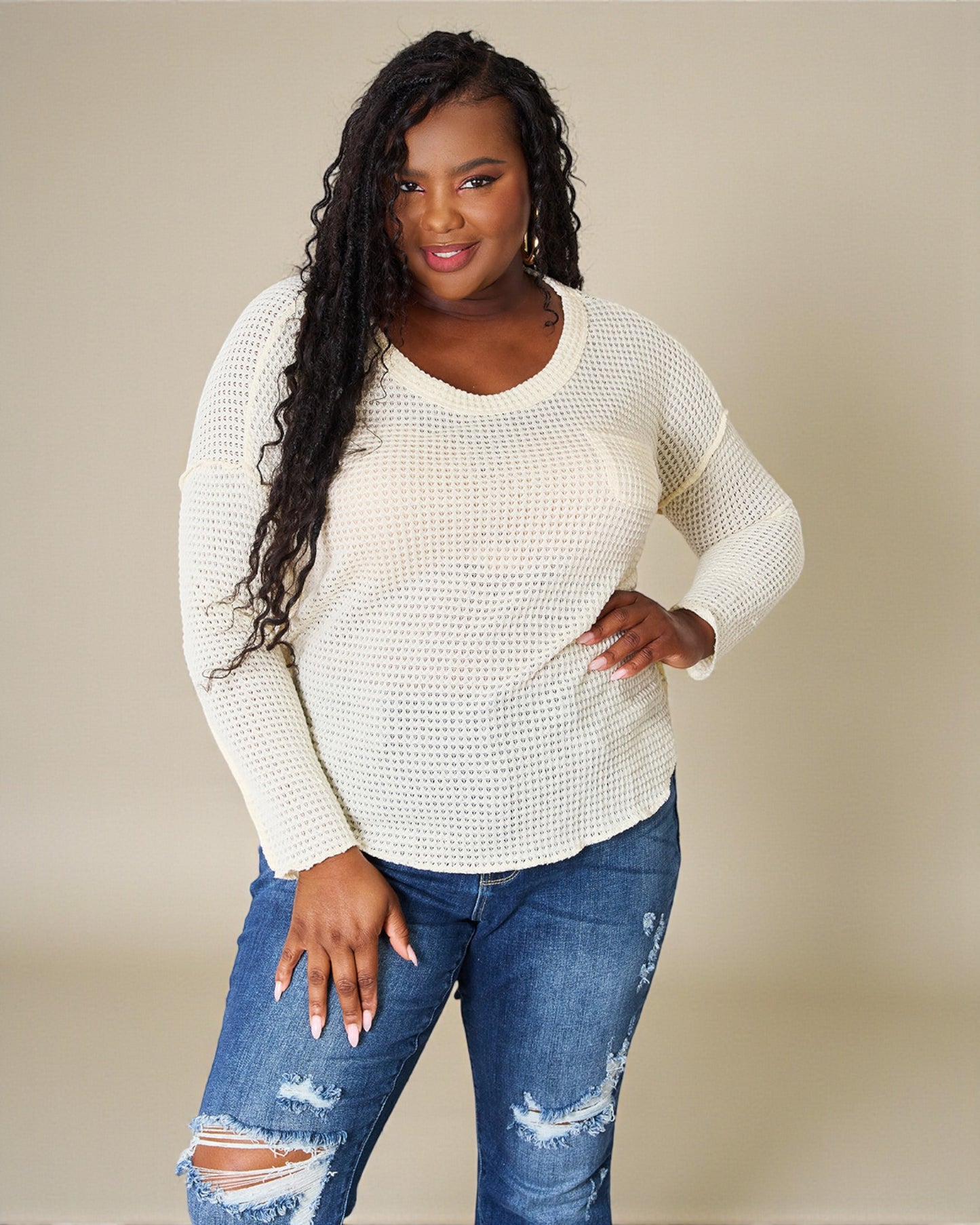 Woman wearing a white sweater and blue jeans against a beige background
