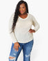 A woman modeling a cream-colored, long-sleeve waffle-knit sweater with a chest pocket, paired with distressed blue jeans, against a plain white background.