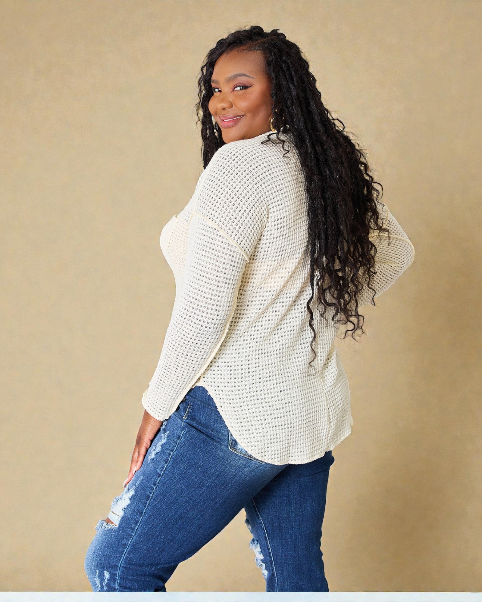 Woman wearing a white textured sweater and blue jeans against a beige background
