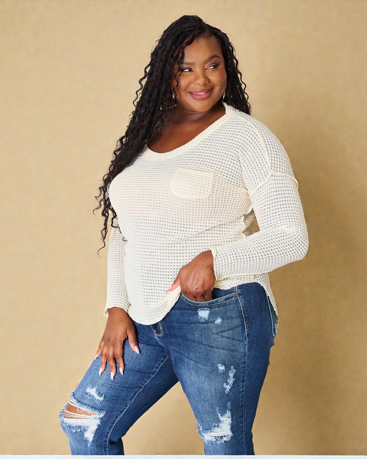 Woman wearing a white long-sleeve top and blue jeans against a beige background