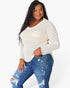 A woman modeling a cream-colored, long-sleeve waffle-knit top with a chest pocket, paired with distressed blue jeans, against a plain white background.
