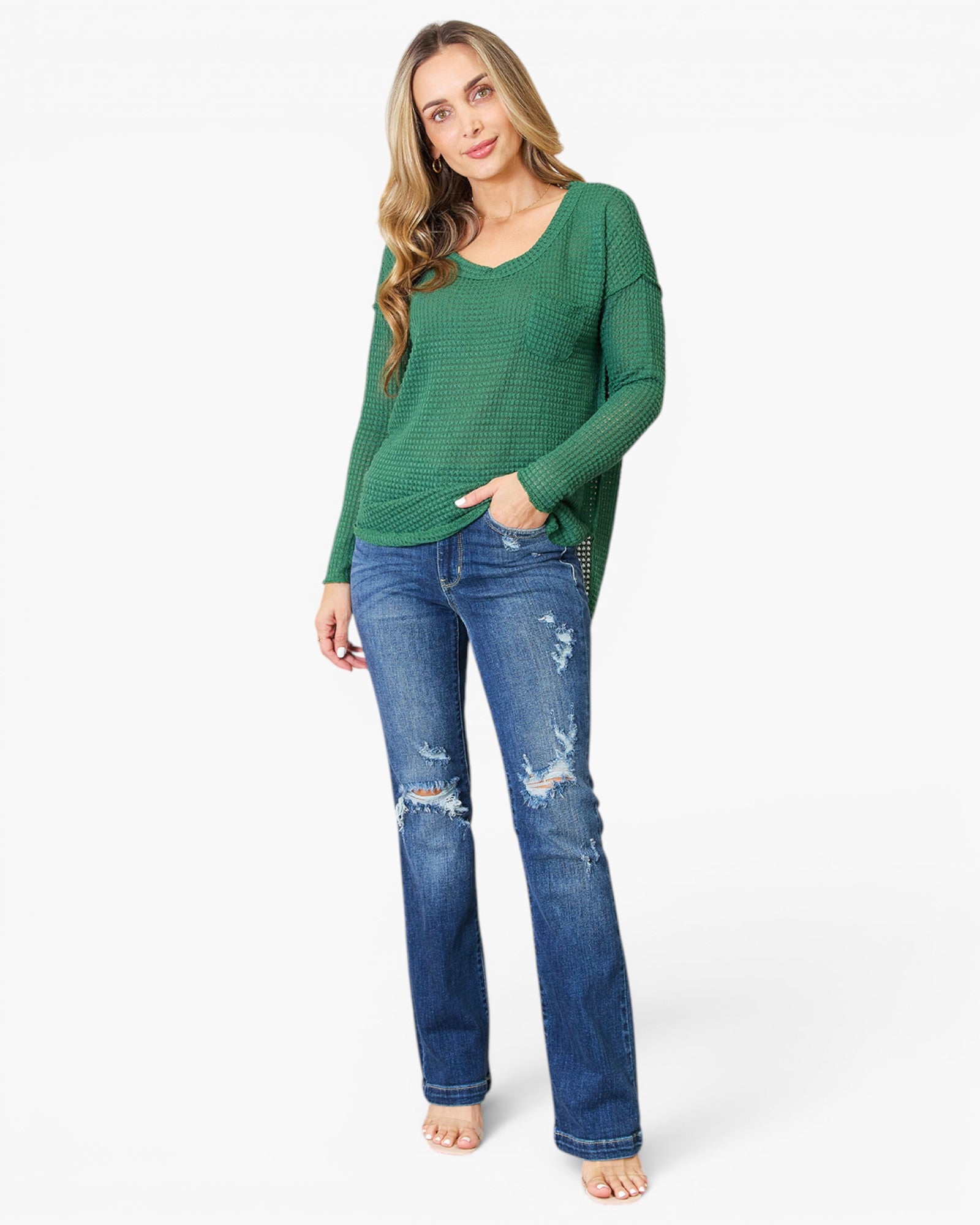 A woman modeling a green long-sleeve waffle-knit top and distressed blue jeans against a plain white studio background.