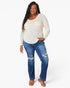 A woman modeling a cream-colored, textured long-sleeve top with a chest pocket, paired with distressed blue jeans and tan sandals, against a plain white studio background.
