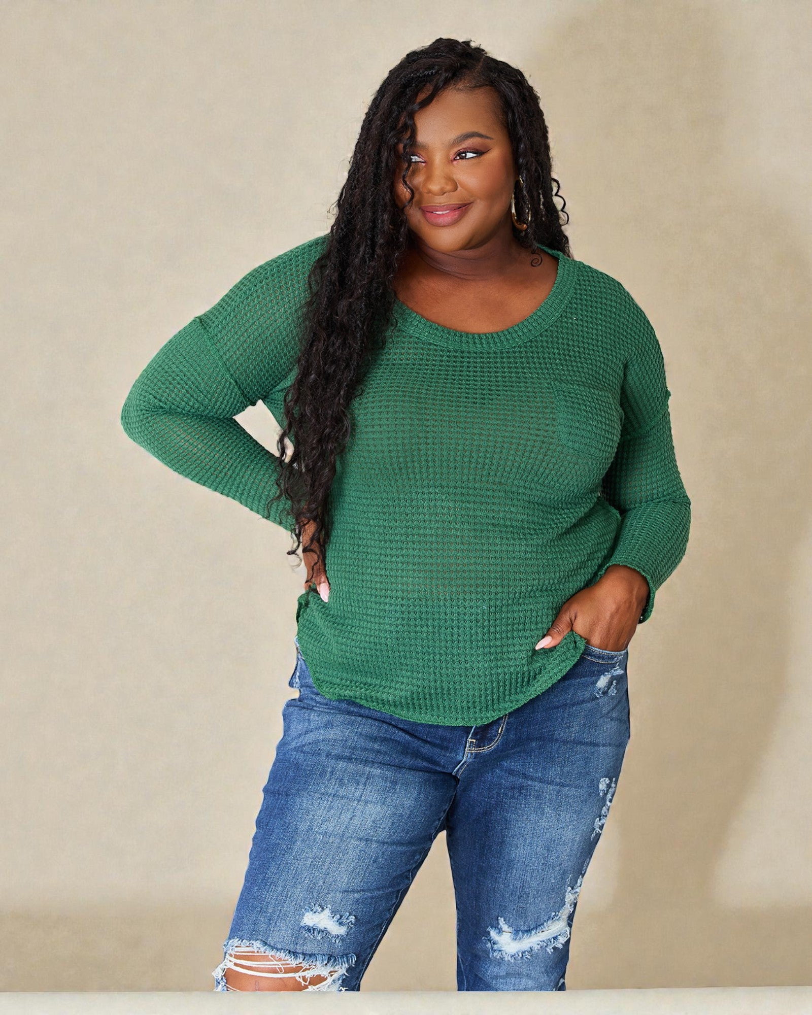 Woman wearing a green sweater and blue jeans against a beige background