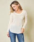 Woman wearing a beige sweater and blue jeans against a plain background