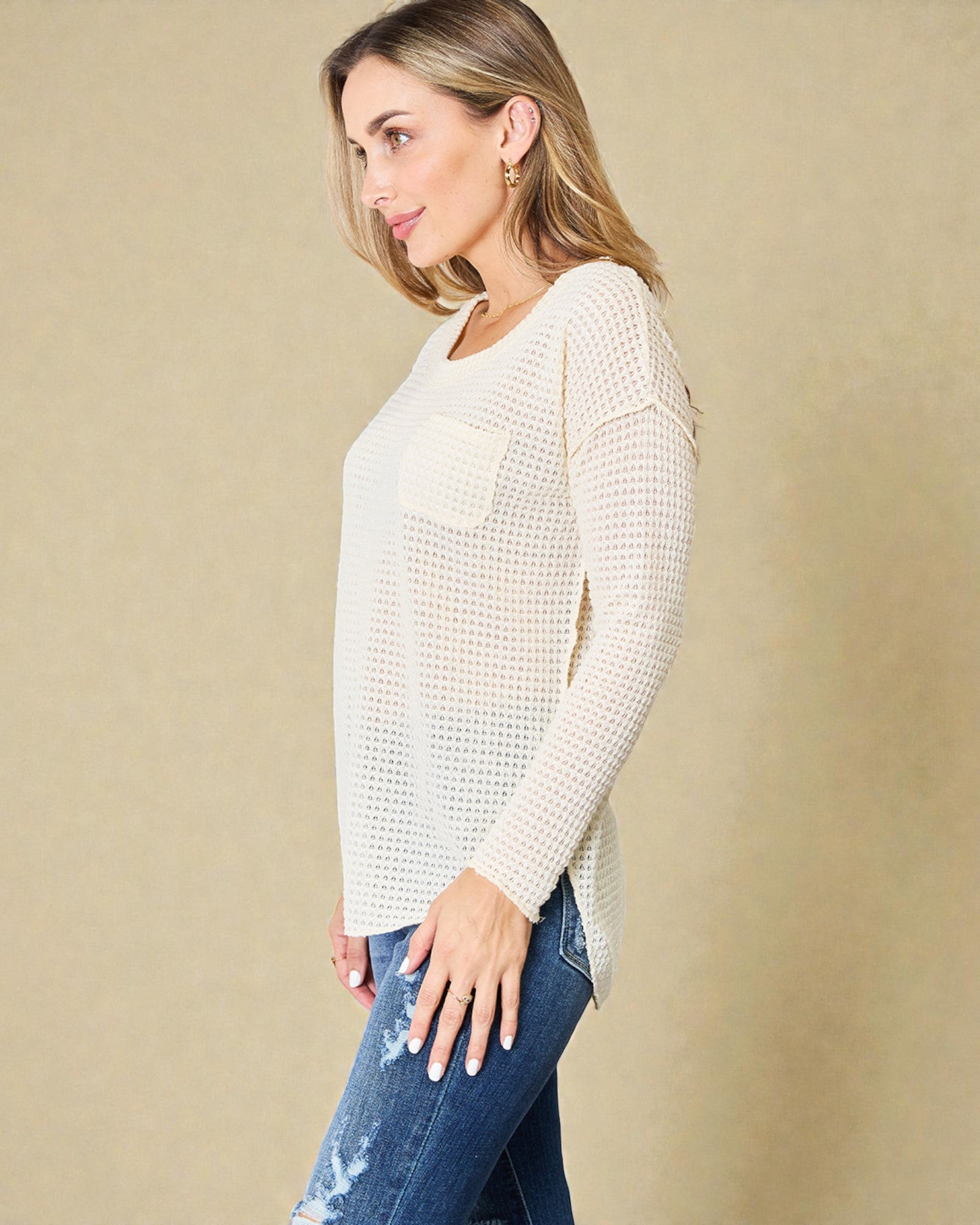 Woman wearing a light-colored sweater and blue jeans against a beige background