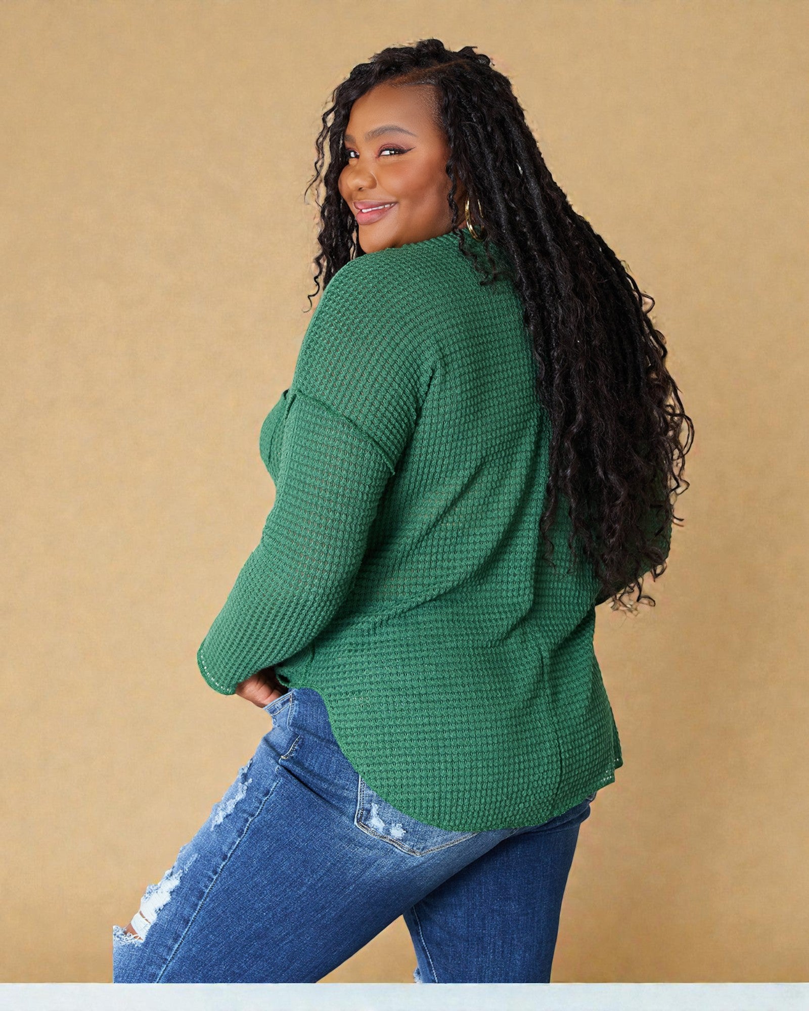 Woman wearing a green textured sweater and blue jeans against a beige background