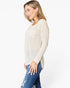 A woman wearing a cream-colored, long-sleeve waffle-knit top with a chest pocket, paired with blue jeans, shown in profile against a plain white background.