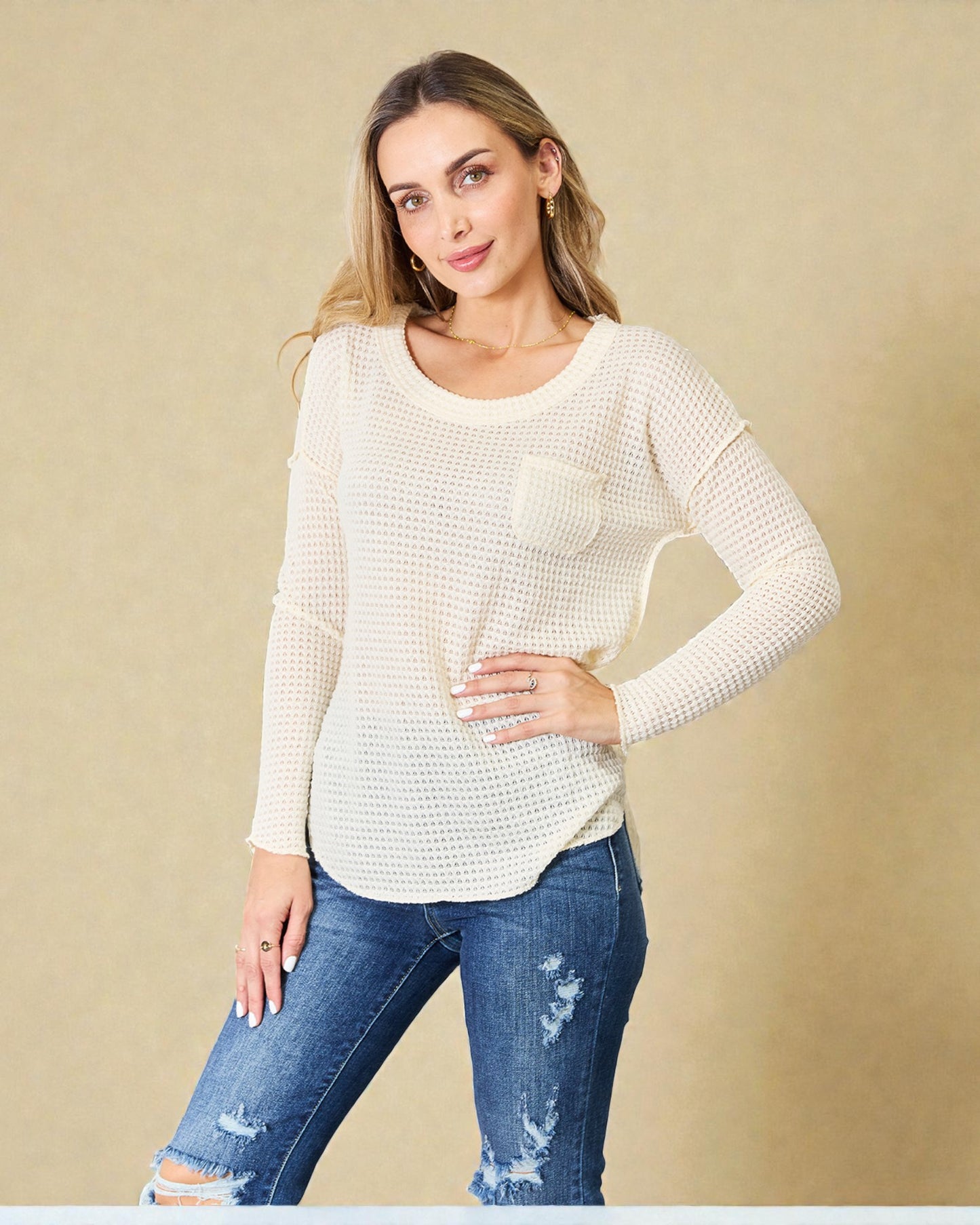 Woman wearing a white textured sweater and blue jeans against a beige background