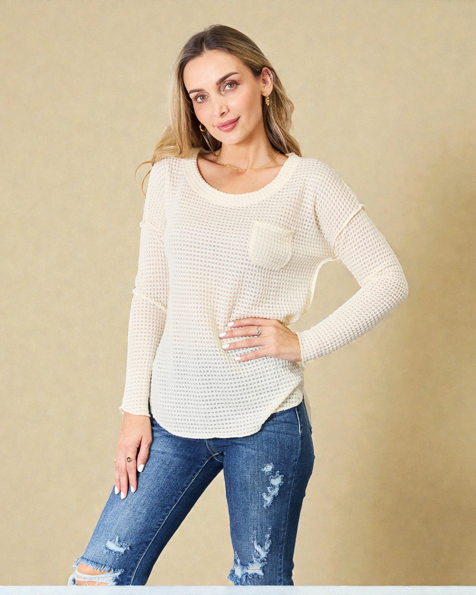 Woman wearing a white textured sweater and blue jeans against a beige background