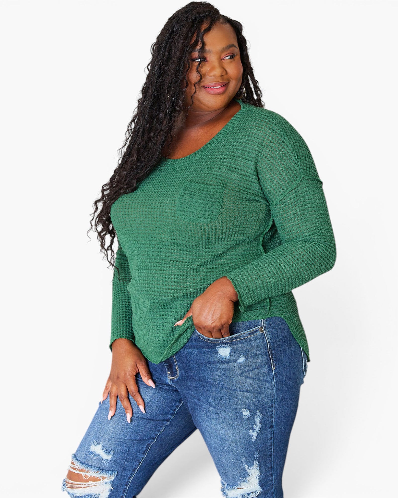 A woman modeling a green waffle-knit long-sleeve top with a chest pocket, paired with distressed blue jeans, against a plain white background.