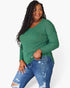 A woman modeling a green waffle-knit long-sleeve top with a chest pocket, paired with distressed blue jeans, against a plain white background.